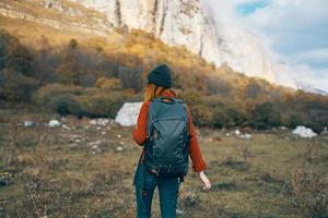 en resande i en Tröja med en ryggsäck på henne tillbaka värma hatt landskap höst bergen foto