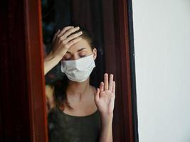kvinna med stängd ögon i medicinsk mask ser ut de fönster. låsning foto