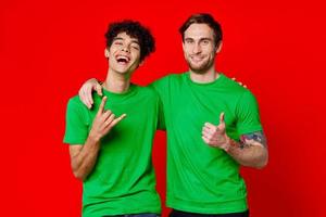 två män kramas i grön t-tröjor på en röd bakgrund foto