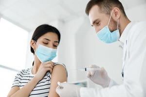 en läkare injicerar en vaccin till en kvinna patient i en medicinsk mask foto