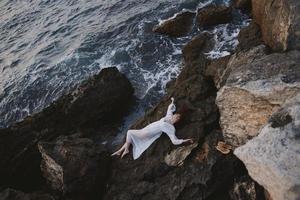 kvinna i lång vit klänning våt hår liggande på en klippig klippa landskap foto