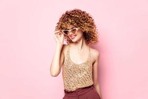 skön kvinna lockigt hår solglasögon leende rosa bakgrund foto