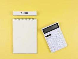 platt layout av öppnad tom sida anteckningsbok med trä- kalender april och vit kalkylator på gul bakgrund. en gång i månaden finansiell planen begrepp. foto