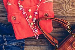 kvinnors Kläder och Tillbehör Tröja, jeans, handväska, pärlor på trä- bakgrund. tonad bild. foto