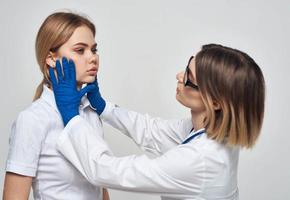 kvinna läkare i en medicinsk klänning och i blå handskar med en stetoskop runt om henne nacke och en kvinna patient foto