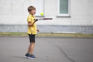 barn med en tennis racket och en boll. pojke tennis spelare. skol går i för sporter foto