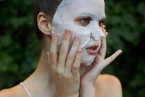 skön kvinna vit mask se till de sida och ha kvar din händer nära din ansikte kosmetologi buskar i de bakgrund foto