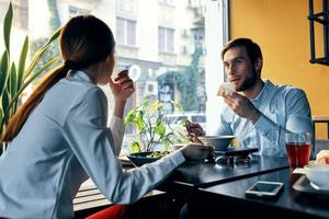 en kvinna i en ljus skjorta och en företag man ha lunch på en tabell i en Kafé utsökt mat drycker anställda foto