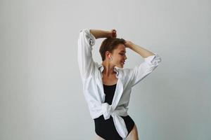 ung kvinna tonåring lyssnande till musik med ofruktbar hörlurar och dans Hem, flin med tänder med en kort frisyr i en vit skjorta på en vit bakgrund. flicka naturlig poser med Nej filter foto