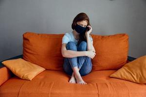 ledsen kvinna Sammanträde på de orange soffa på Hem i skyddande masker livsstil foto