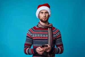 stilig man i en santa hatt med en telefon i hans händer blå bakgrund foto