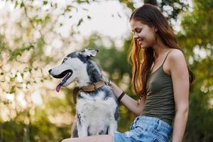 en kvinna med en hes ras hund ler och kärleksfullt stroke henne älskad hund medan gående i natur i de parkera i höst mot de bakgrund av solnedgång foto