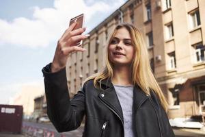 modern kvinna bär läder jacka utomhus nära de byggnad blond färsk luft foto