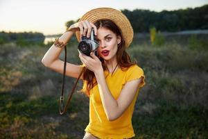 kvinna innehav kamera utseende in i de kamera lins röd mun hatt natur färsk luft foto