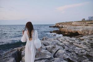 kvinna i vit klänning stenar hav promenad tillbaka se foto