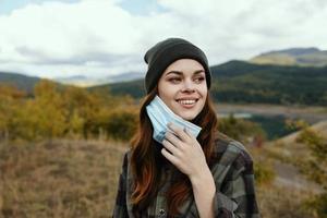 Lycklig kvinna med en medicinsk mask i henne hand på natur i de skog foto