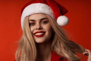 Söt kvinna i santa hatt leende kosmetika glamour röd bakgrund foto