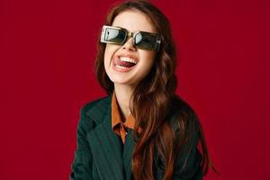 glad kvinna som visar tunga grimas solglasögon röd bakgrund foto