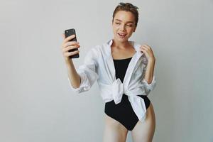 Tonårs flicka bloggare tar foton och skott. själv på video på henne telefon för social media innehåll, video bloggare, selfies mot en vit vägg med en leende på Hem, frilansare