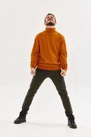 en stark man i ett orange Tröja, byxor och stövlar dans på en ljus bakgrund foto