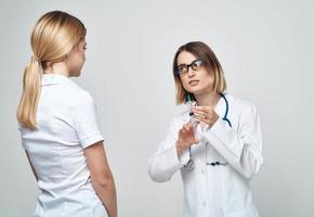 en kvinna sjuksköterska innehar en spruta i henne hand på en ljus bakgrund med en stetoskop och en kvinna patient foto