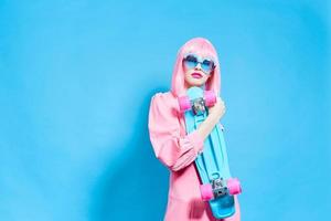 porträtt av en kvinna med skateboard i rosa peruk blå bakgrund foto