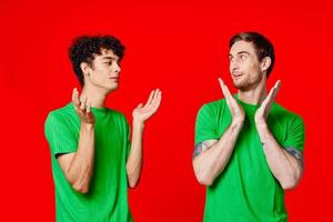 två män innehav deras huvuden i grön t-tröjor på en röd bakgrund foto