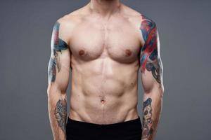 sportig man med pumpade upp magmuskler tatueringar på hans vapen grå bakgrund muskler foto