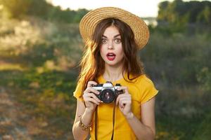 förälskad kvinna innehav en kamera i henne händer hatt röd mun gul t-shirt färsk luft foto
