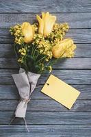 bukett av gul blommor med tom papper kort som en märka för namn eller hälsningar på trä- bakgrund foto