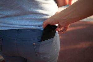 närbild av en man är hand stjäl en mobil telefon med en jeans ficka. foto