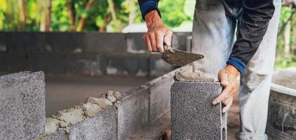 hand av arbetstagare putsning cement på tegel vägg på konstruktion webbplats foto