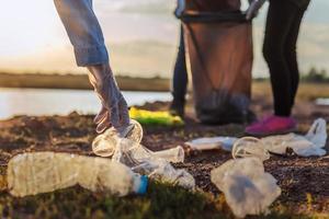 människor volontär- förvaring sopor plast flaska in i svart väska på parkera nära flod i solnedgång foto