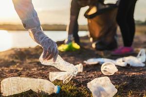 människor volontär- förvaring sopor plast flaska in i svart väska på parkera flod i solnedgång foto