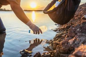 människor volontär- förvaring sopor plast flaska in i svart väska på flod i solnedgång foto