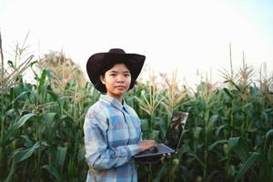 ung kvinna stående använda sig av bärbar dator kontroll majs i odla. teknologi lantbruk begrepp foto