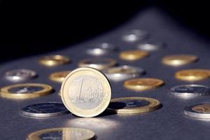 ett euro mynt stående på kant lysande i strålkastare mot många annorlunda mynt på mörk bakgrund. pengar strömma foto
