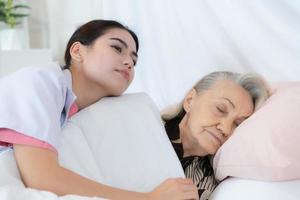 vårdgivare för ett äldre kvinna filt de äldre kvinna på de säng efter slutföra de varje vecka hälsa kolla upp på de patientens Hem foto