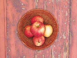 röda äpplen på en korgplatta på en träbordbakgrund foto