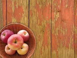 röda äpplen på en korgplatta på en träbordbakgrund foto