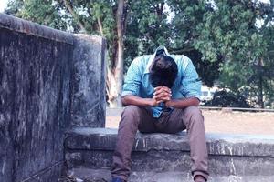 rangpur, bangladesh 2023. deprimerad tonåring man Sammanträde ensam på vägg i utomhus.obehagligt smärta. ledsen olycklig stilig man.bangladeshi och Asien pojke lidande depression. foto