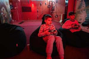 två Pojkar spelare spela gamepad video spel trösta i röd gaming rum. foto