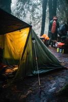 vildmark överlevnad. bushcraft tält under de presenning i tung regn, fattande de kyla av gryning. en scen av uthållighet och elasticitet foto