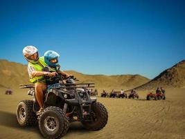 de glad ung familj Sammanträde på de atvs i de öken- foto