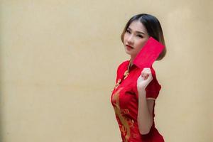 porträtt skön asiatisk kvinna i Cheongsam klänning, thailand människor, glada kinesisk ny år koncept, glad asiatisk lady i kinesisk traditionell klänning innehav en röd kuvert foto