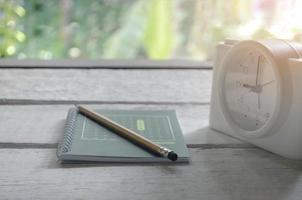 grön bok, penna och väckarklocka på ett vitt träbord