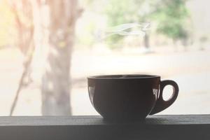 närbild av en brun kaffekopp med rök på ett träbord med utsikt över träd foto
