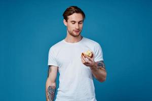 söt kille med en tatuering och i en vit t-shirt på en blå bakgrund äter äpplen beskurna se foto