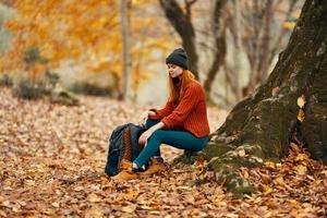 kvinna Sammanträde nära en träd i höst skog och faller löv landskap parkera foto