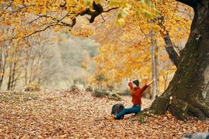 kvinna med en ryggsäck under en träd i de parkera och faller löv höst landskap foto